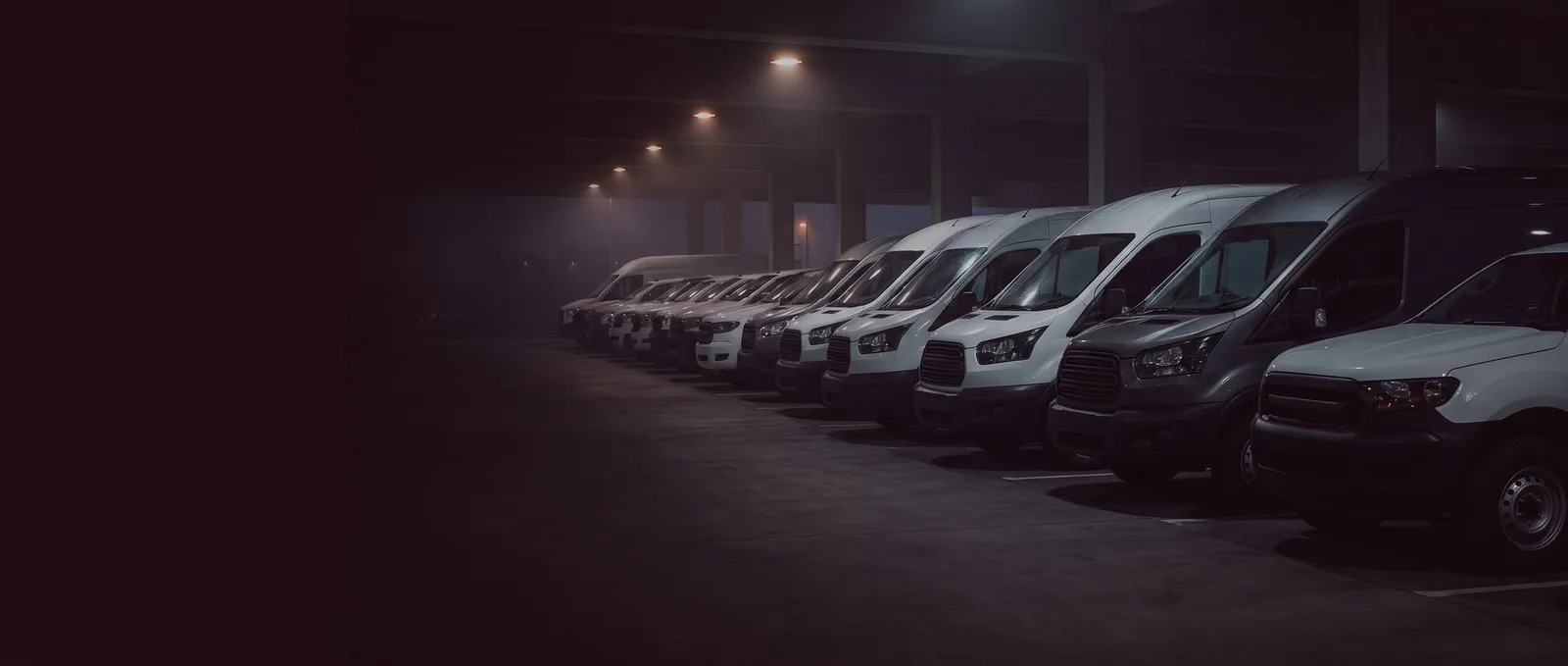 Fileira de vans e utilitários estacionados lado a lado dentro de uma garagem, à noite