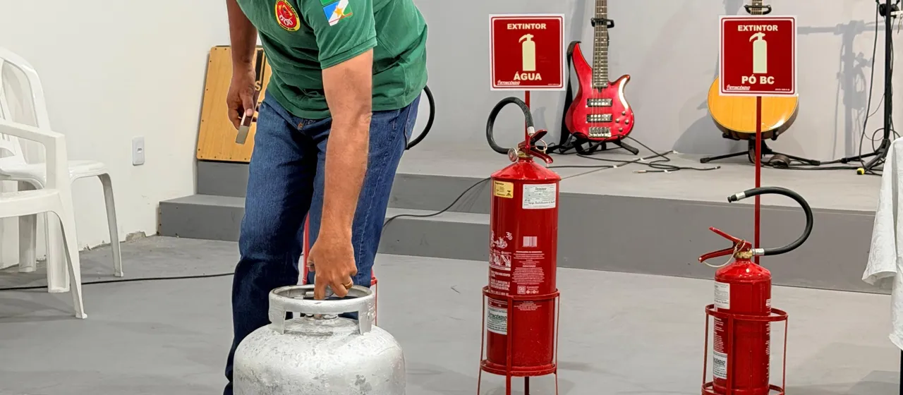 Miguel Arcanjo Lopes Neto preparando a demonstração prática com botijão de gás, ao lado das placas de extintor de água e de pó BC